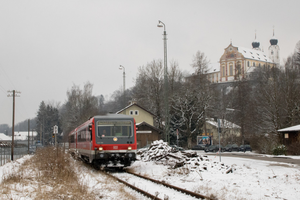 628 566 vor dem Bahnhofsgebäude in Altenmark auf der Traun-Alz-Bahn, im Hintergrund ist das Kloster Baumburg, aufgenommen am 20.03.2018.